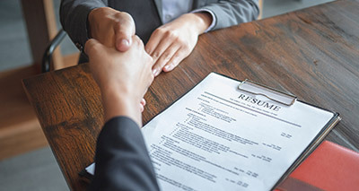 A Sports Job applicant and an Interviewer shake hands above a resume, which rests on a stained wood table.